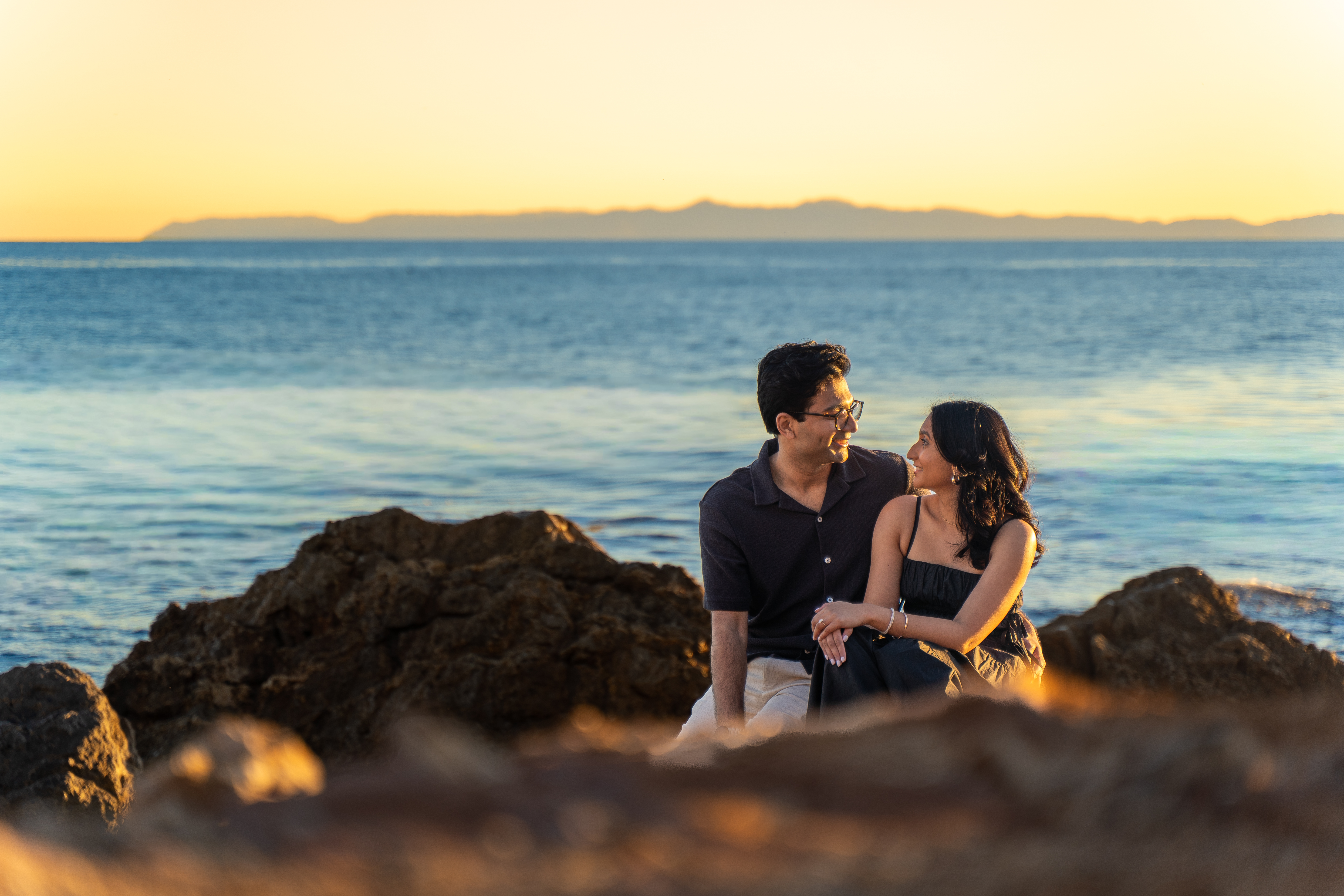 Neesha and Mandar sitting on the rocks at sunset, looking at each other